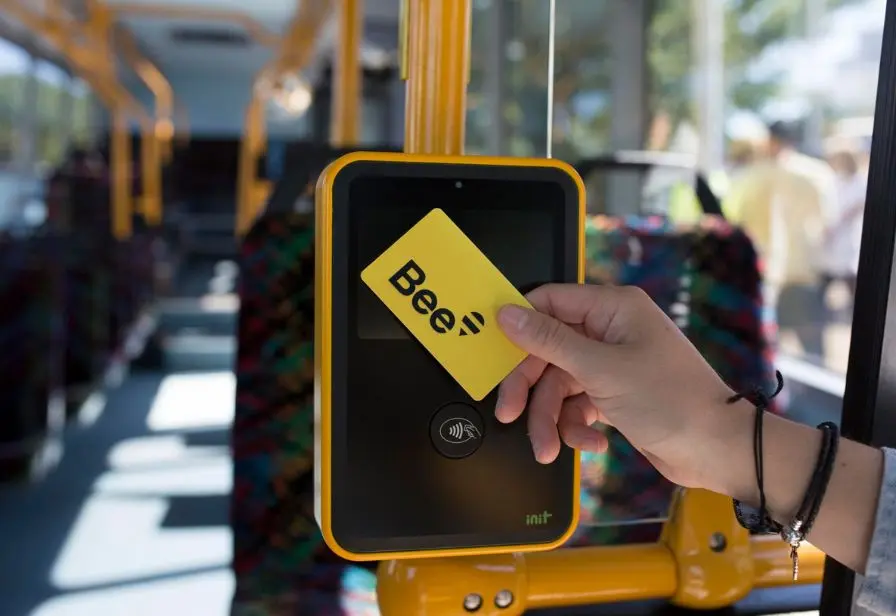 Image of a person holding up a Bee Card to a bus reader to get on the bus